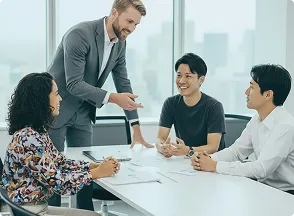 会議の様子。外国人男性が立って話しながら座っている男性2人と女性1が笑顔で聞いている